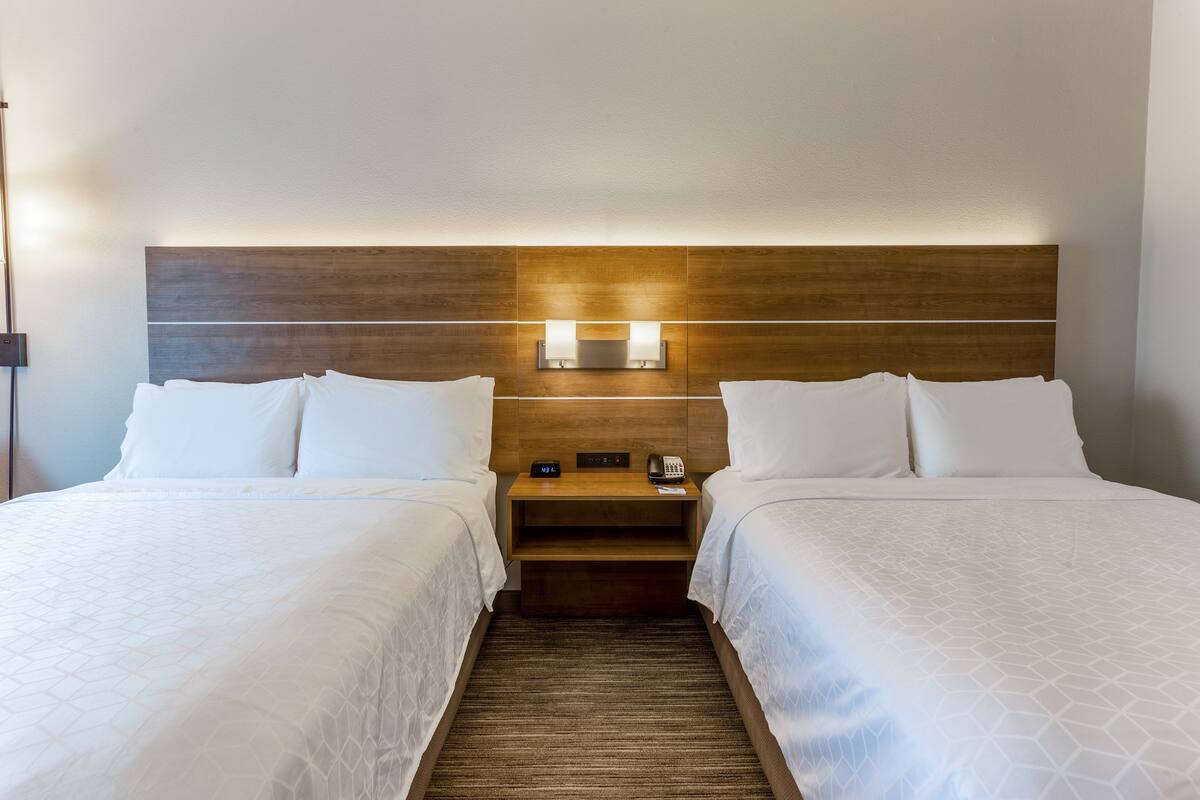 A hotel room with two beds, a wooden headboard, bedside lamps, a nightstand, and a carpeted floor.