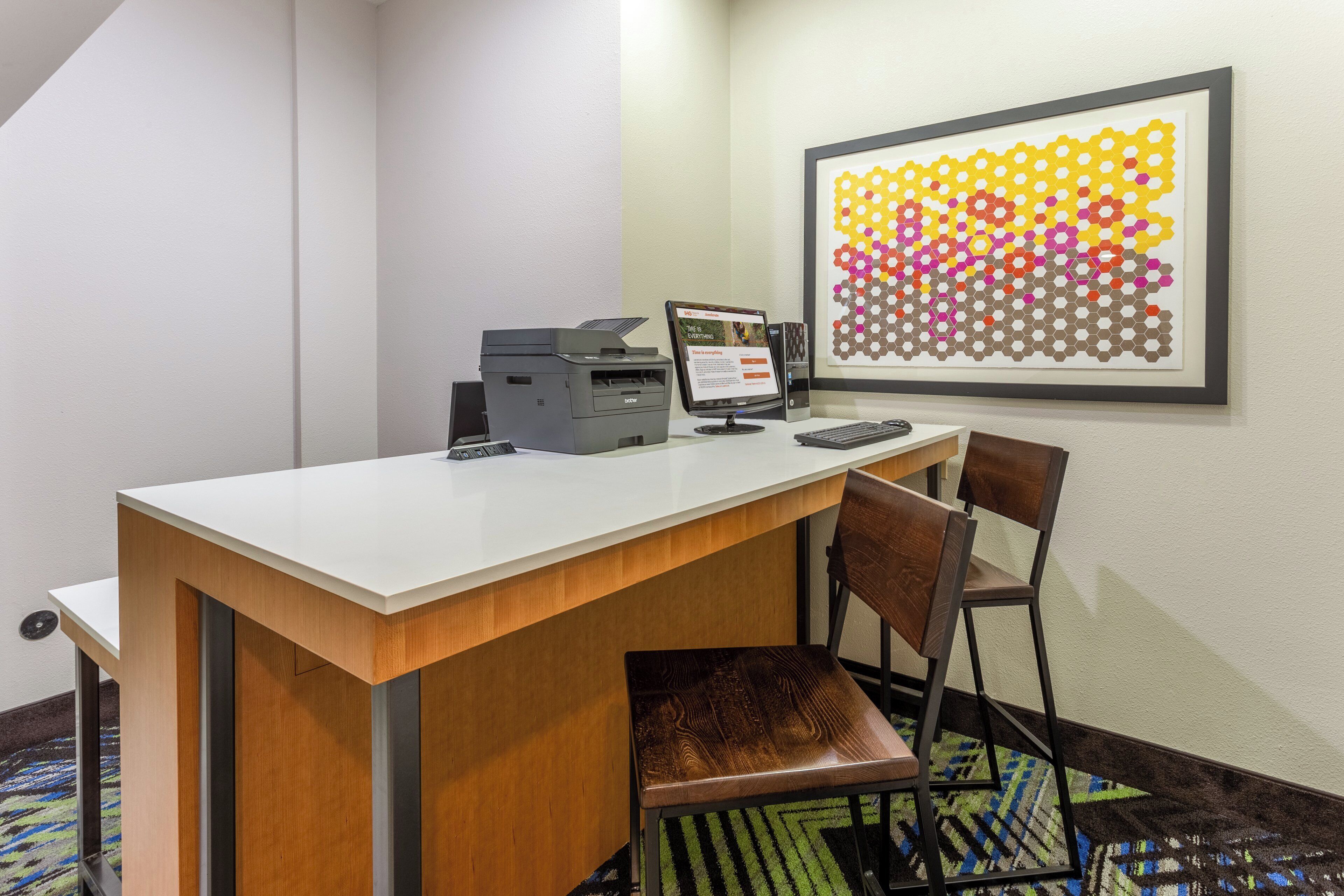 A hotel office with a desk, computer, printer, and a colorful hexagonal wall art.