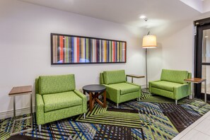 Una habitación con sillas tapizadas en verde, una mesa redonda, una obra de arte colorida con rayas y una alfombra estampada.