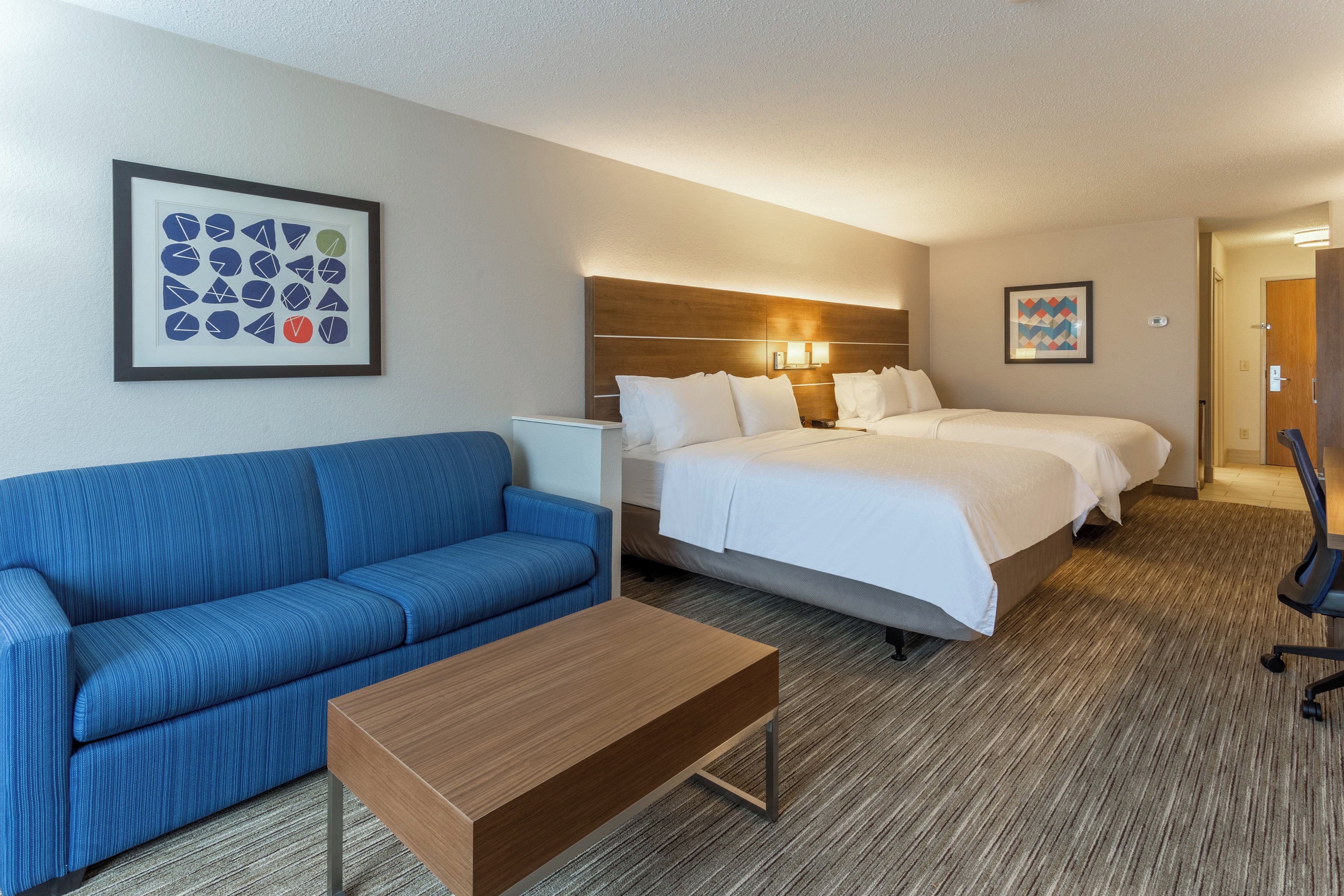 A hotel room with a blue sofa, a wooden coffee table, a double bed with white bedding, and two bedside tables.