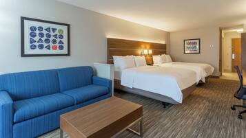 A hotel room with a blue sofa, a wooden coffee table, a double bed with white bedding, and two bedside tables.