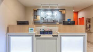 Un comptoir d’accueil d’hôtel au design moderne, doté d’un écran numérique et d’une enseigne indiquant « Holiday Inn Express & Suites ».