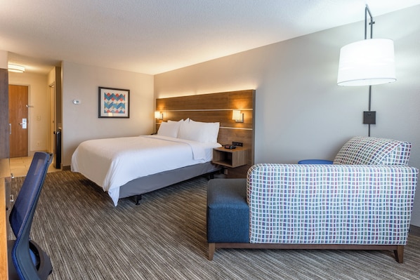 A hotel room with a bed, bedside table, lamp, chair, and a wall-mounted picture.