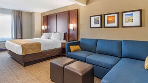 A hotel room with a bed, a sofa, and a small table. There are three framed pictures on the wall.