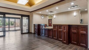A spacious hotel lobby with a wooden floor, a reception desk, and a clock on the wall.