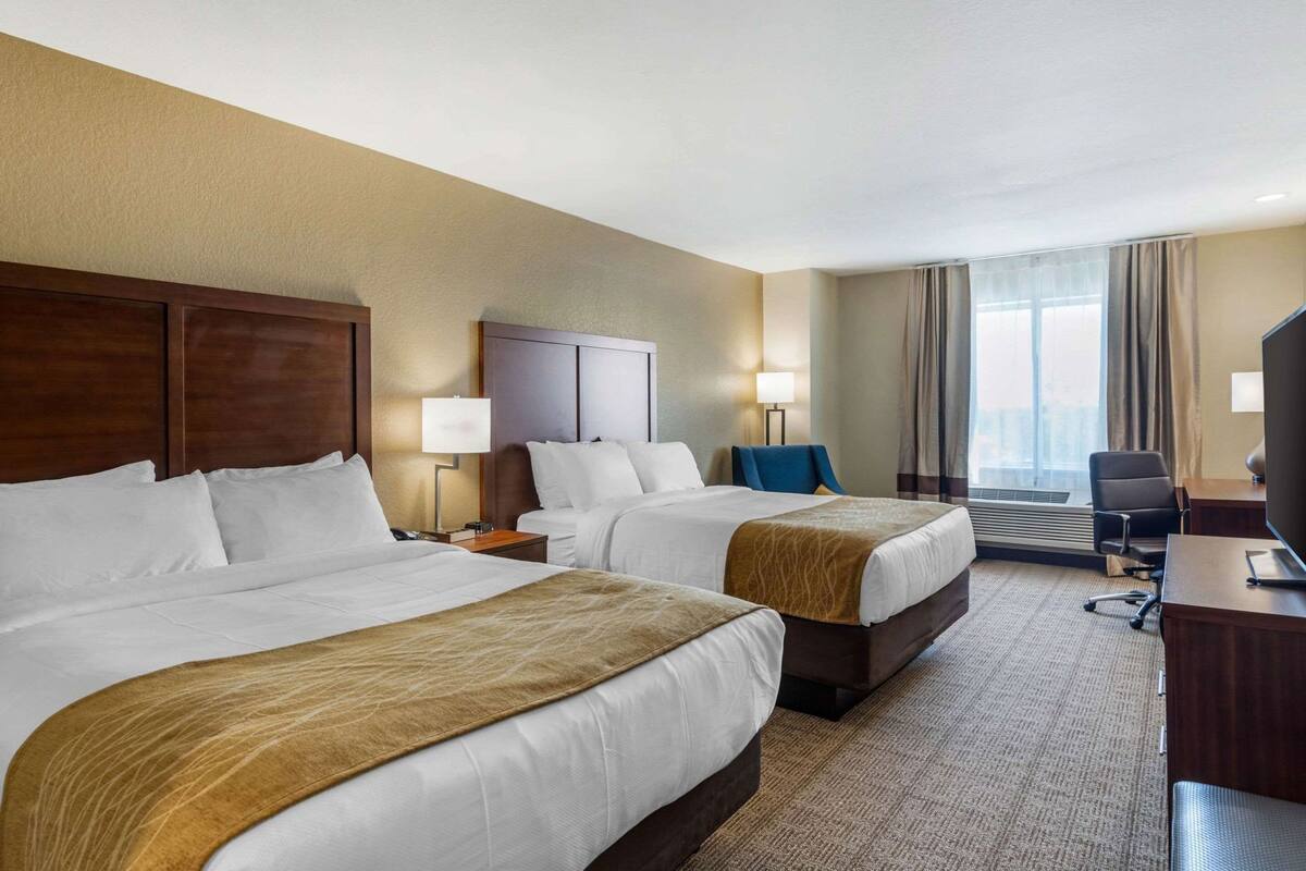 A hotel room with two beds, a desk, a chair, a TV, and a large window.