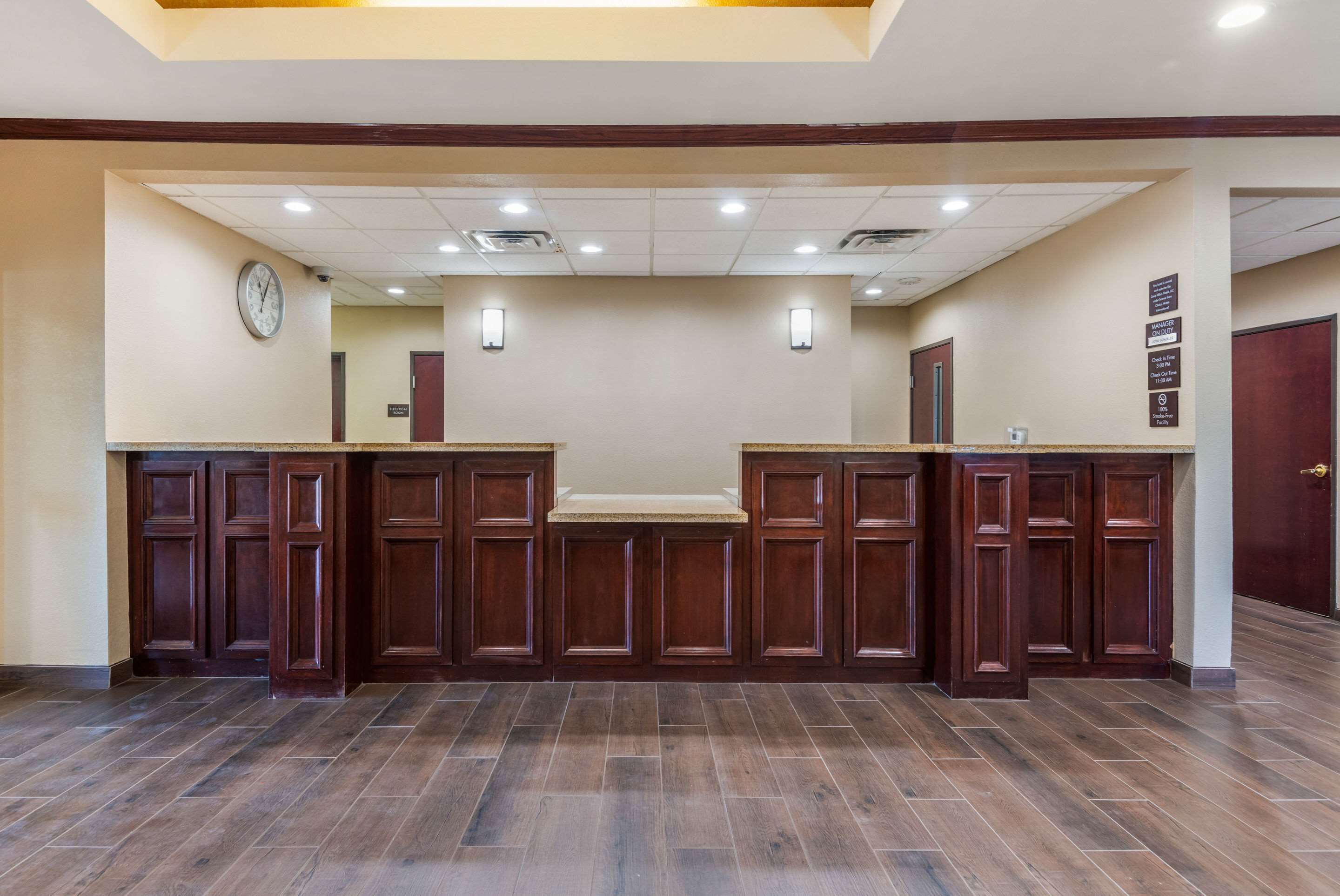 A reception area with a wooden reception desk, a clock on the wall, and a sign with room information.