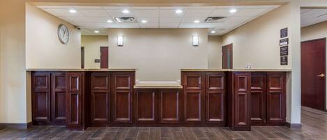 A reception area with a wooden reception desk, a clock on the wall, and a sign with room information.