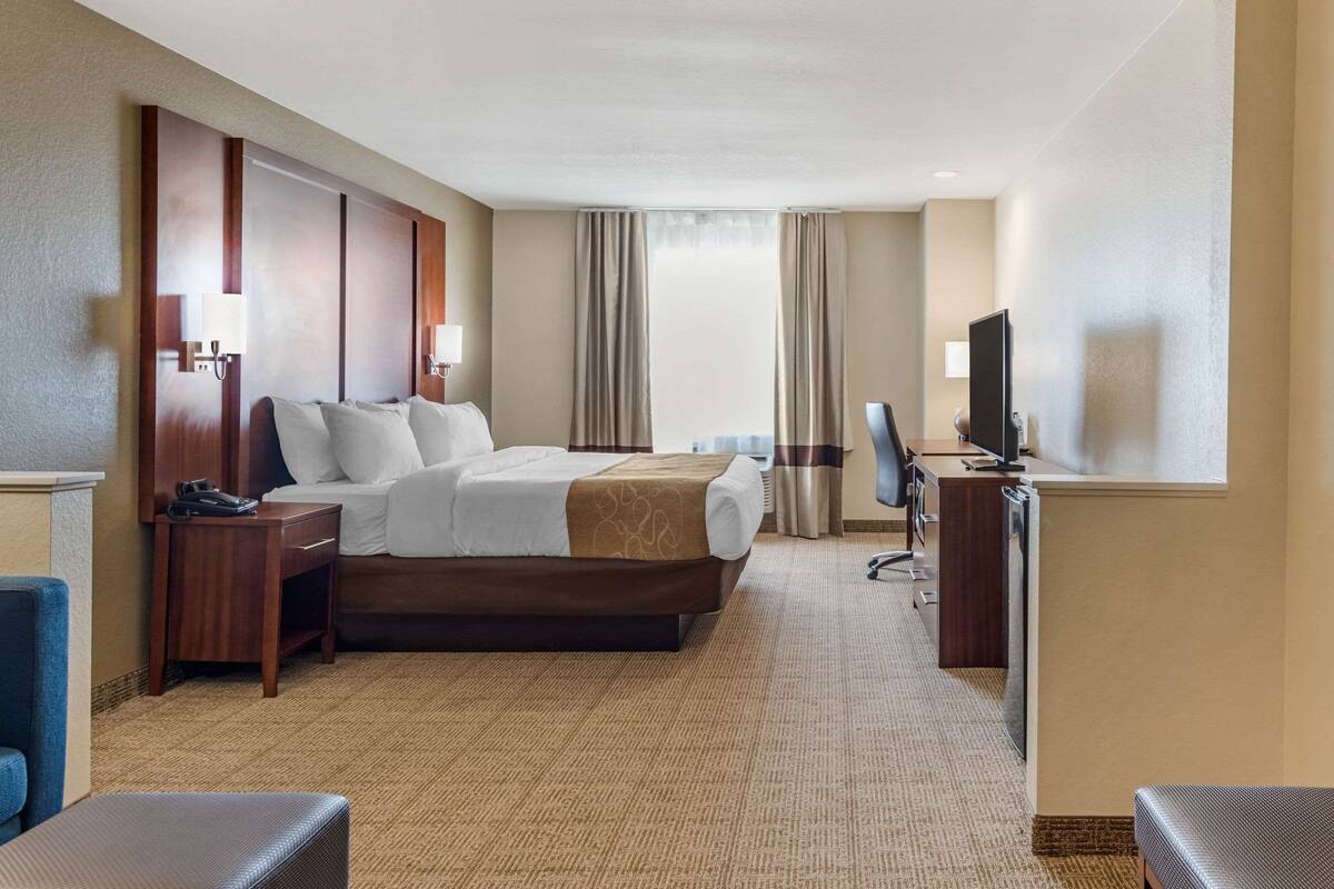 A hotel room with a large bed, a desk, a chair, a television, and a window with curtains.