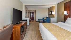 A hotel room with a large bed, a flat-screen TV, a desk with a computer, and a seating area with a sofa and armchairs.
