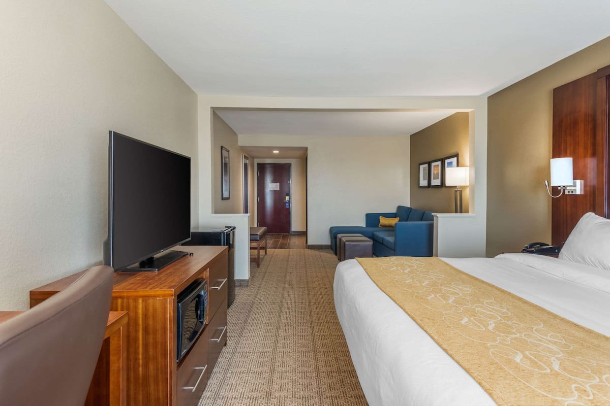 A hotel room with a large bed, a flat-screen TV, a desk with a computer, and a seating area with a sofa and armchairs.