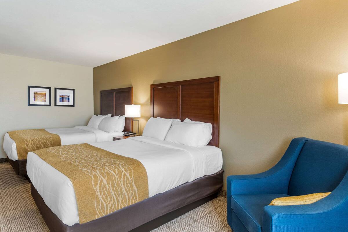 A hotel room with two beds, a blue armchair, and a lamp.