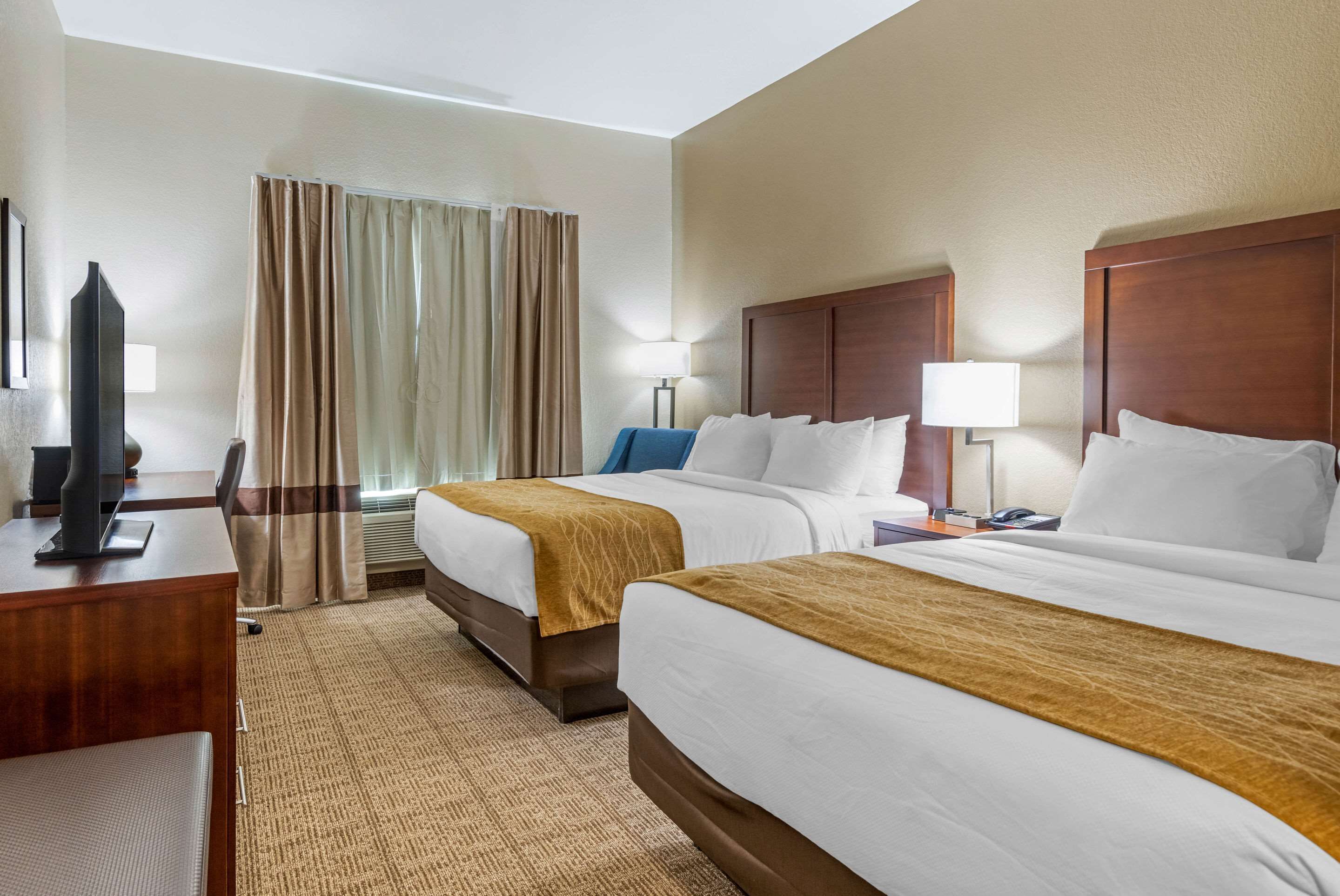 A hotel room with two beds, a desk, a television, and a window with curtains.