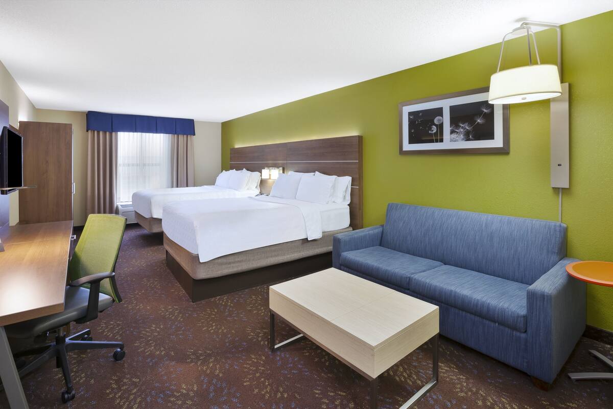 A hotel room with two beds, a sofa, a desk, and a television.