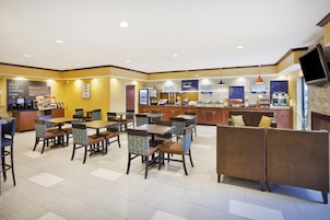 Et morgenmadsområde på hotel med siddepladser, kaffestation og et skranke med udvalg af mad og drikke.