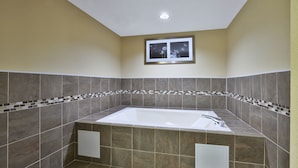A bathroom with a large bathtub, tiled walls, and a small window above the tub.