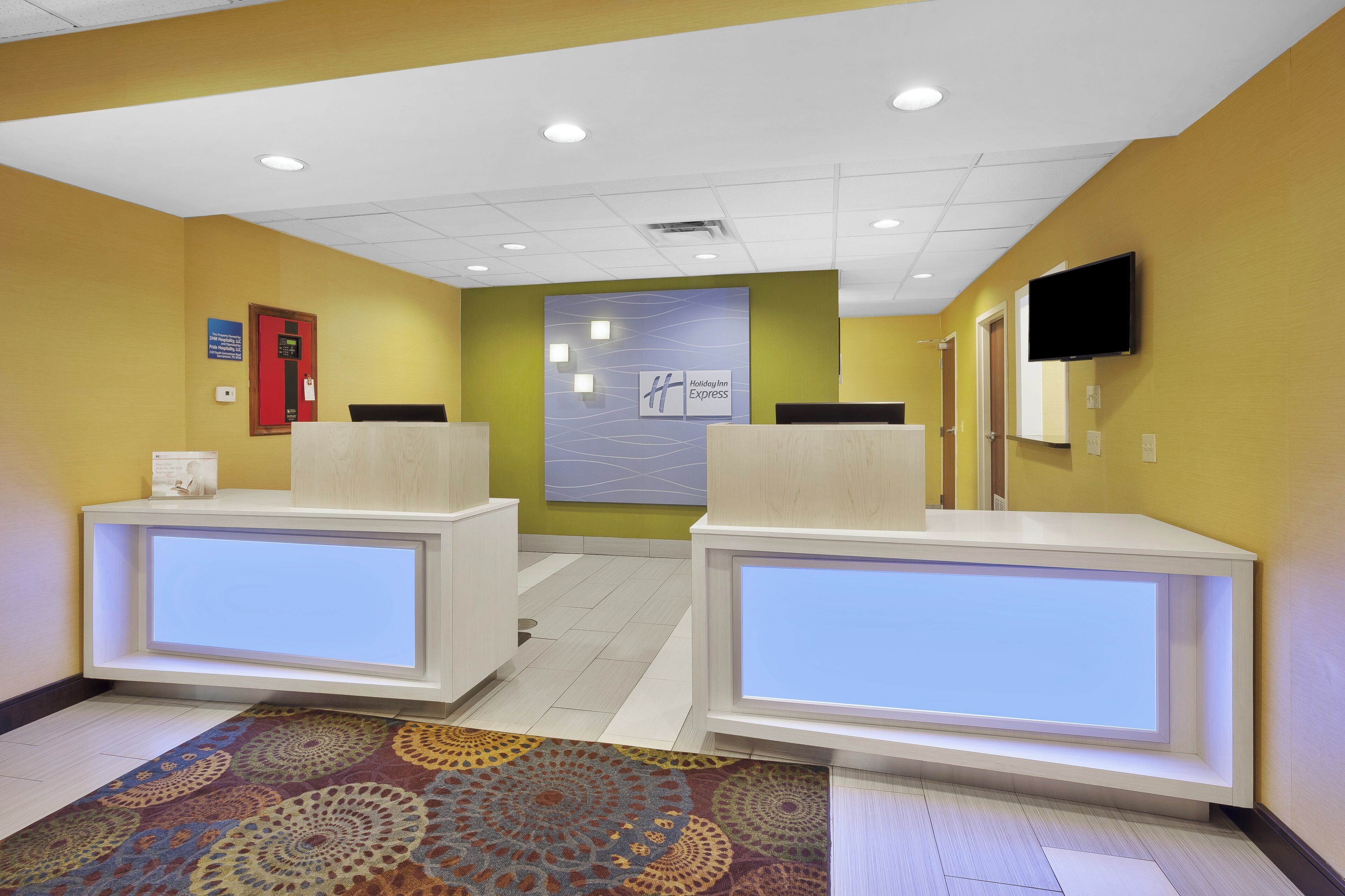 A reception area with two reception desks, a wall-mounted television, and a patterned carpet.
