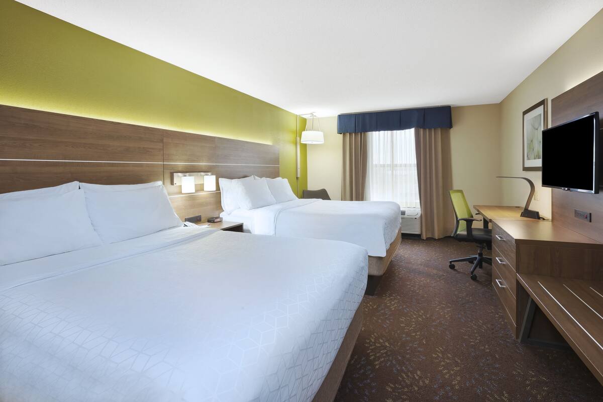A hotel room with two beds, a desk, a chair, a TV, and a window with curtains.