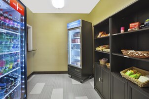 Un área de venta con diversas opciones de bebidas, una sección refrigerada y estantes llenos de aperitivos y artículos de aseo.