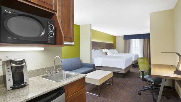 A hotel room with a kitchenette, a bed, a sofa, a desk, and a chair.