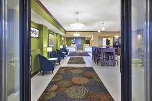 A hotel lobby with a central seating area, a reception desk, and a coffee bar.
