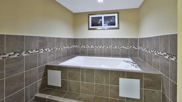 Un baño con una bañera independiente, paredes con azulejos y un pequeño cuadro en la pared.