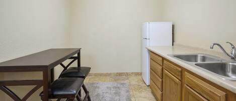 A compact kitchen with a wooden table, two chairs, a refrigerator, and a double sink.