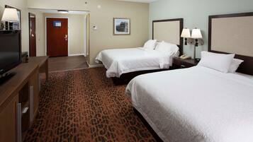 A hotel room with two beds, a television, a desk, and a patterned carpet.