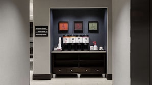 A reception area with a dark wall, framed artwork, a coffee station, and directional signs for the fitness center, board room, and meeting room. - Hampton Inn by Hilton Troy (Troy)