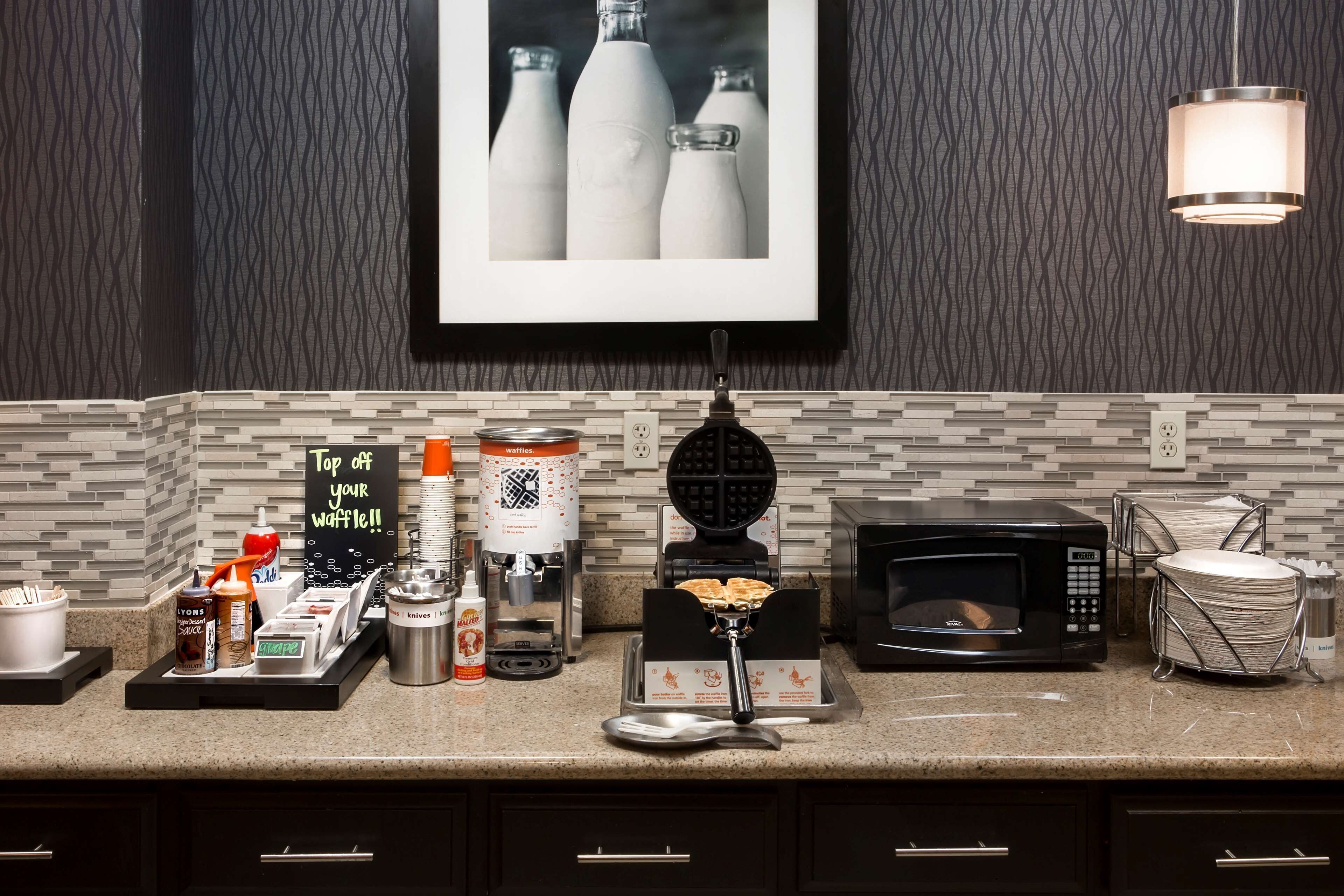 A kitchen counter with a waffle maker, waffle iron, coffee maker, and a microwave.