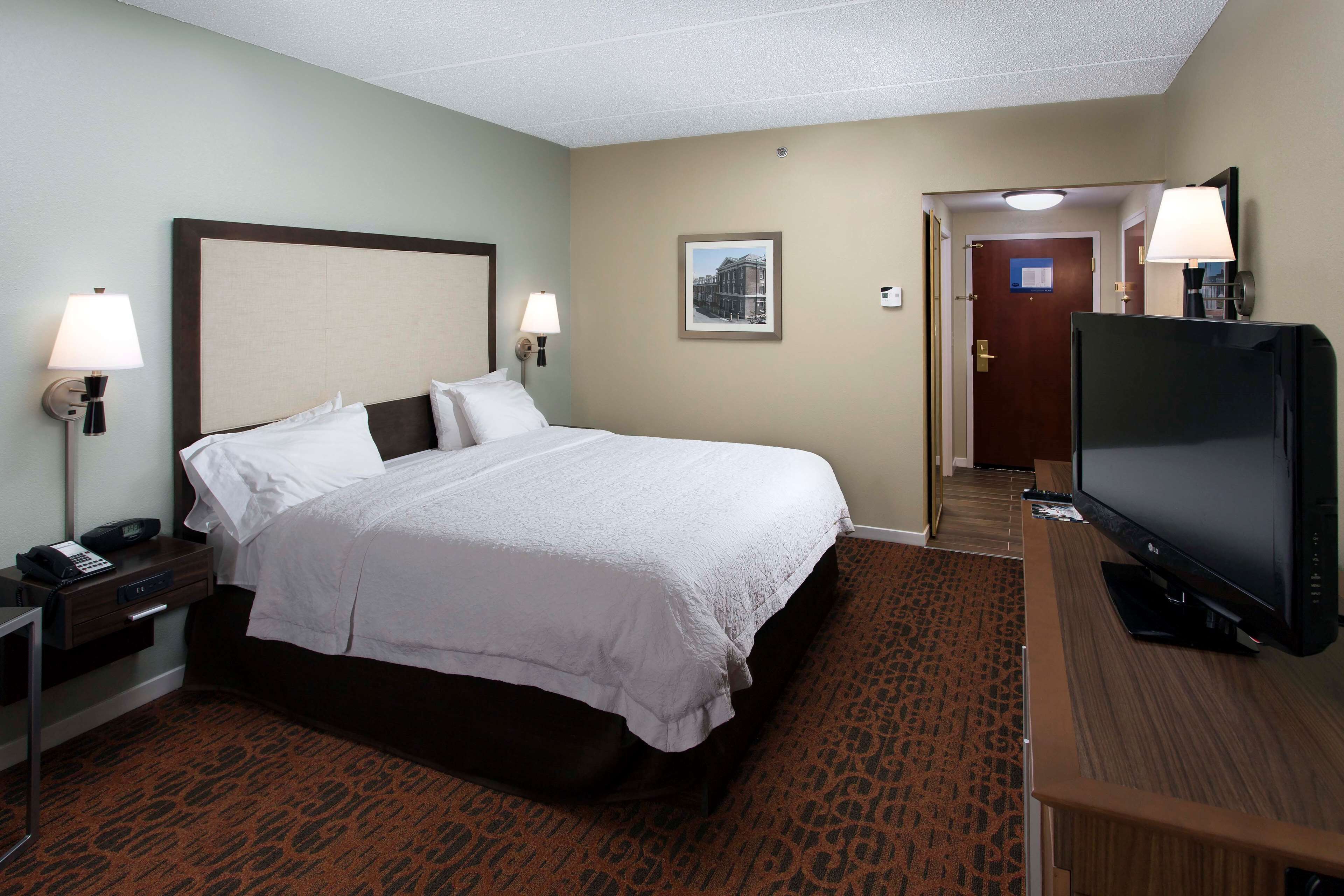 A hotel room with a large bed, bedside lamps, a flat-screen TV, and a carpeted floor.