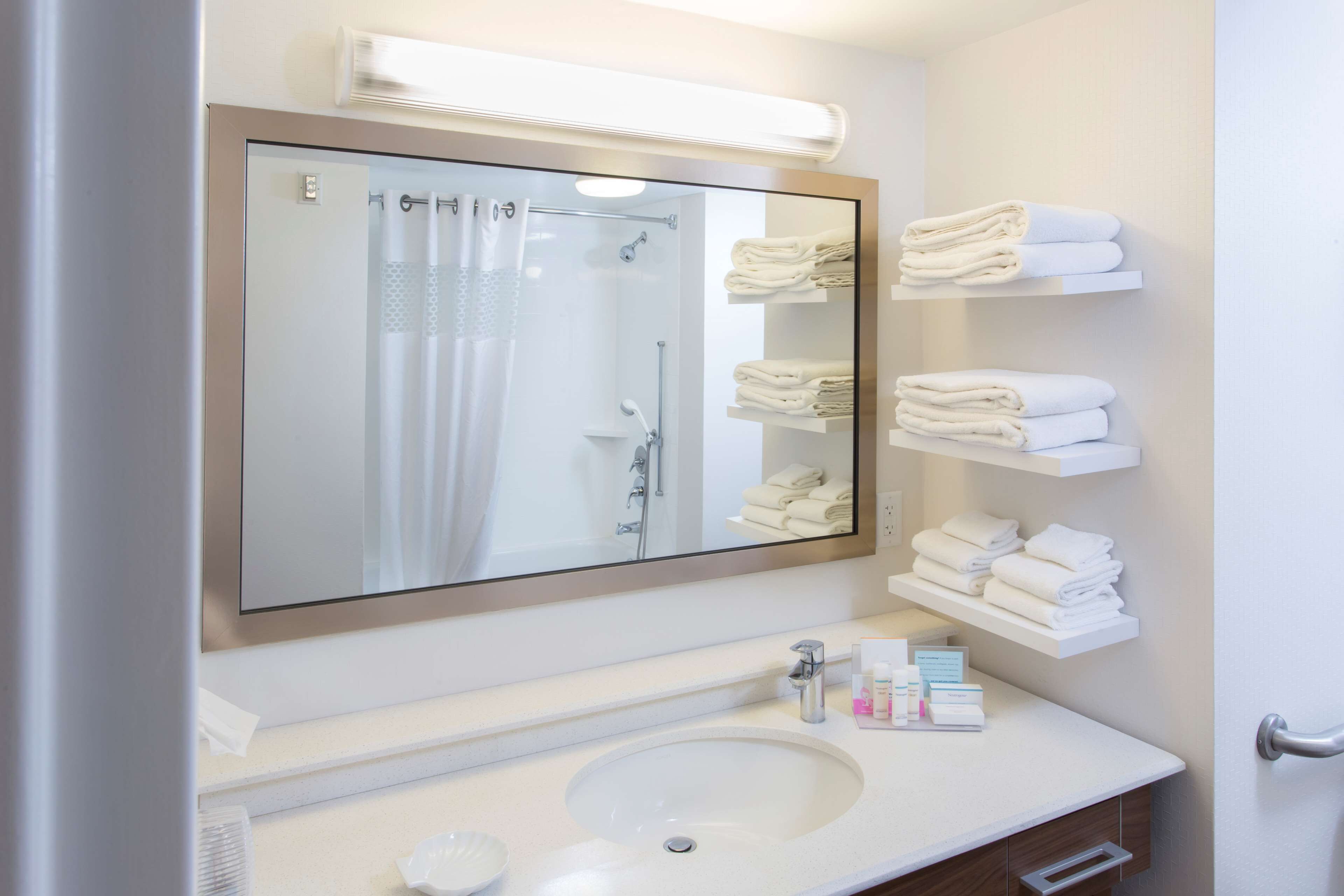 A bathroom with a large mirror, a sink, and shelves with folded towels.