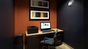A home office setup with a desk, computer, chair, printer, and two framed pictures on the wall.
