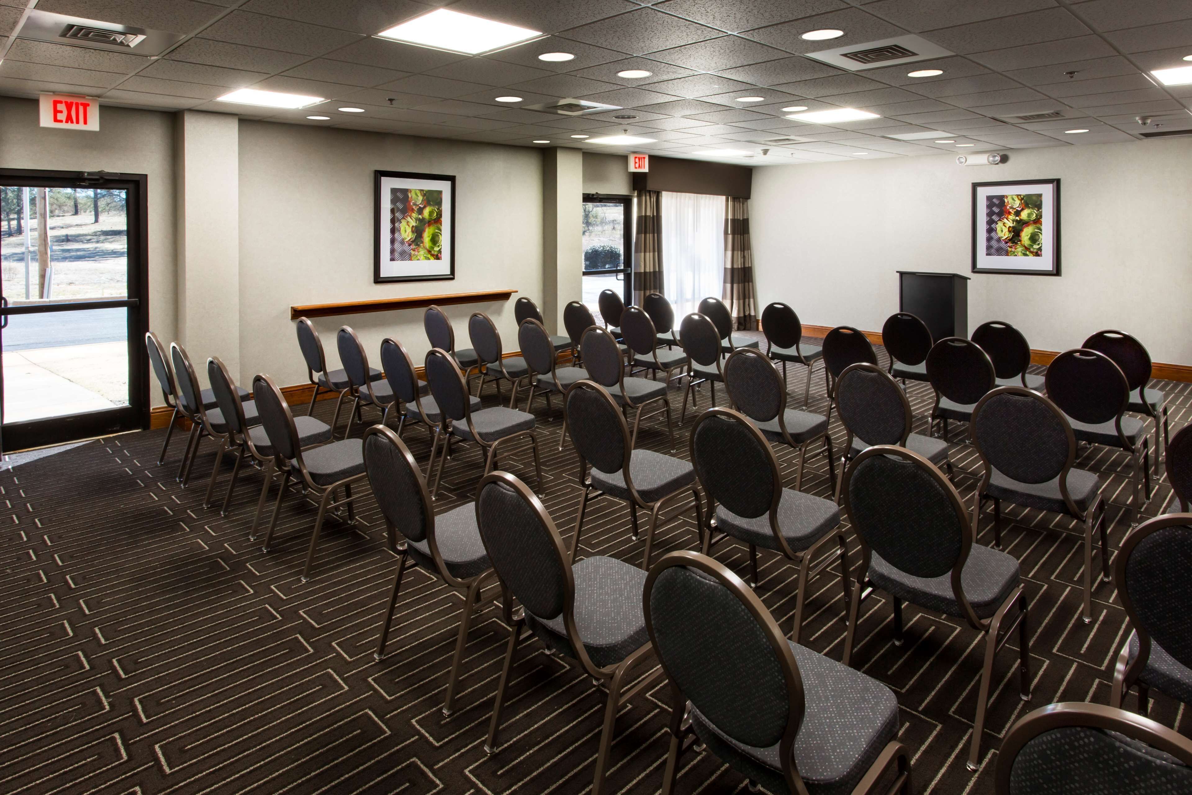 A conference room with rows of chairs, a podium, and exit signs.
