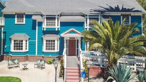 A two-story building with a blue exterior, a red door, and a small porch with chairs. - The Rigdon House (Cambria)