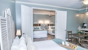 A bedroom with a large bed, a desk, and a chair. There is a door leading to another room. - The Rigdon House (Cambria)