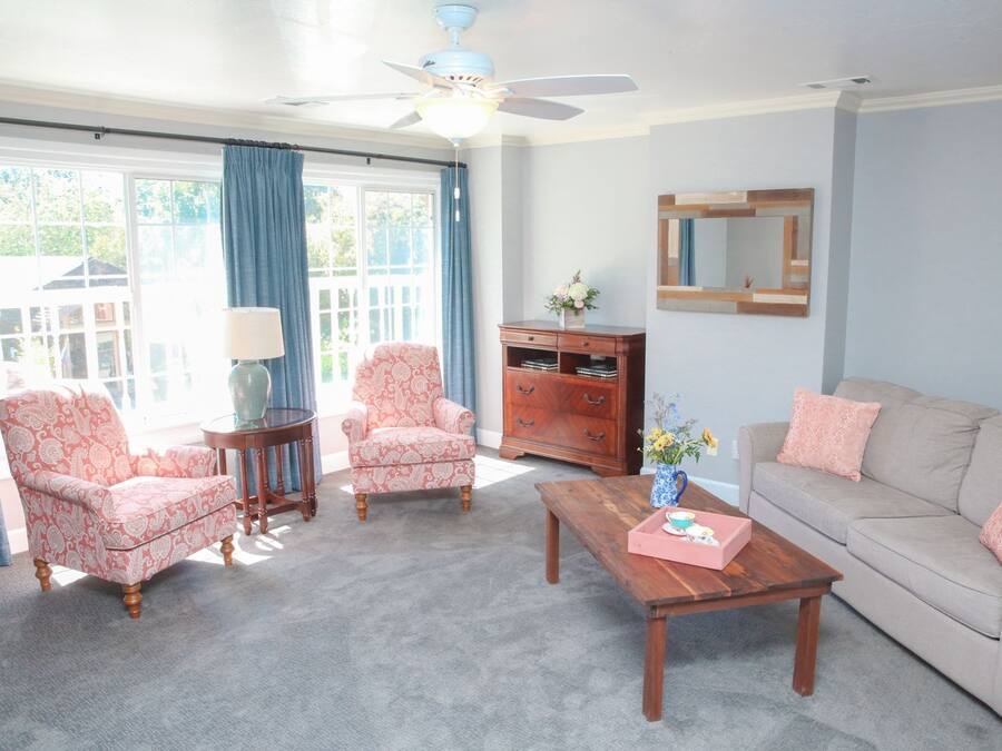 Un salon comprenant un canapé, deux fauteuils, une table basse, une table d’appoint, une lampe, une commode et un ventilateur de plafond.