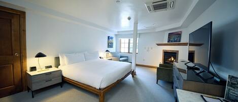 Een moderne hotelkamer met een groot bed, nachtkastjes, een bureau met een flatscreen-televisie, een open haard en een groot raam.