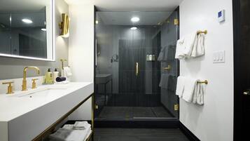A modern bathroom with a white vanity, gold fixtures, a glass-enclosed shower, and neatly arranged towels.