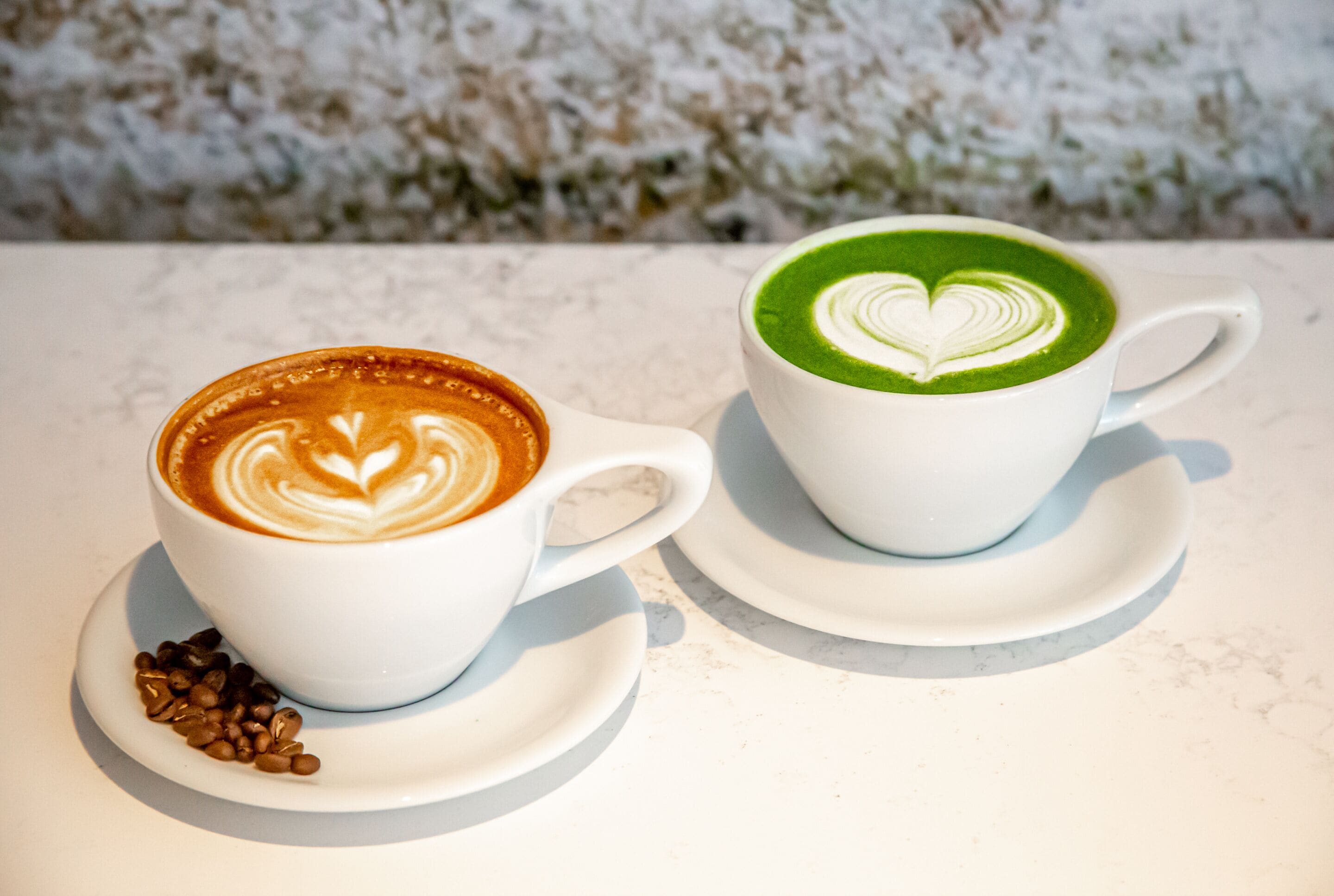 Deux tasses à café blanches ornées de motifs en forme de cœur, posées sur une surface en marbre.
