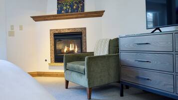 Una habitación con chimenea, un sillón verde, un aparador de madera y un televisor de pantalla plana en la pared.