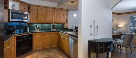 A modern kitchen with wooden cabinets, stainless steel appliances, and a black side table.