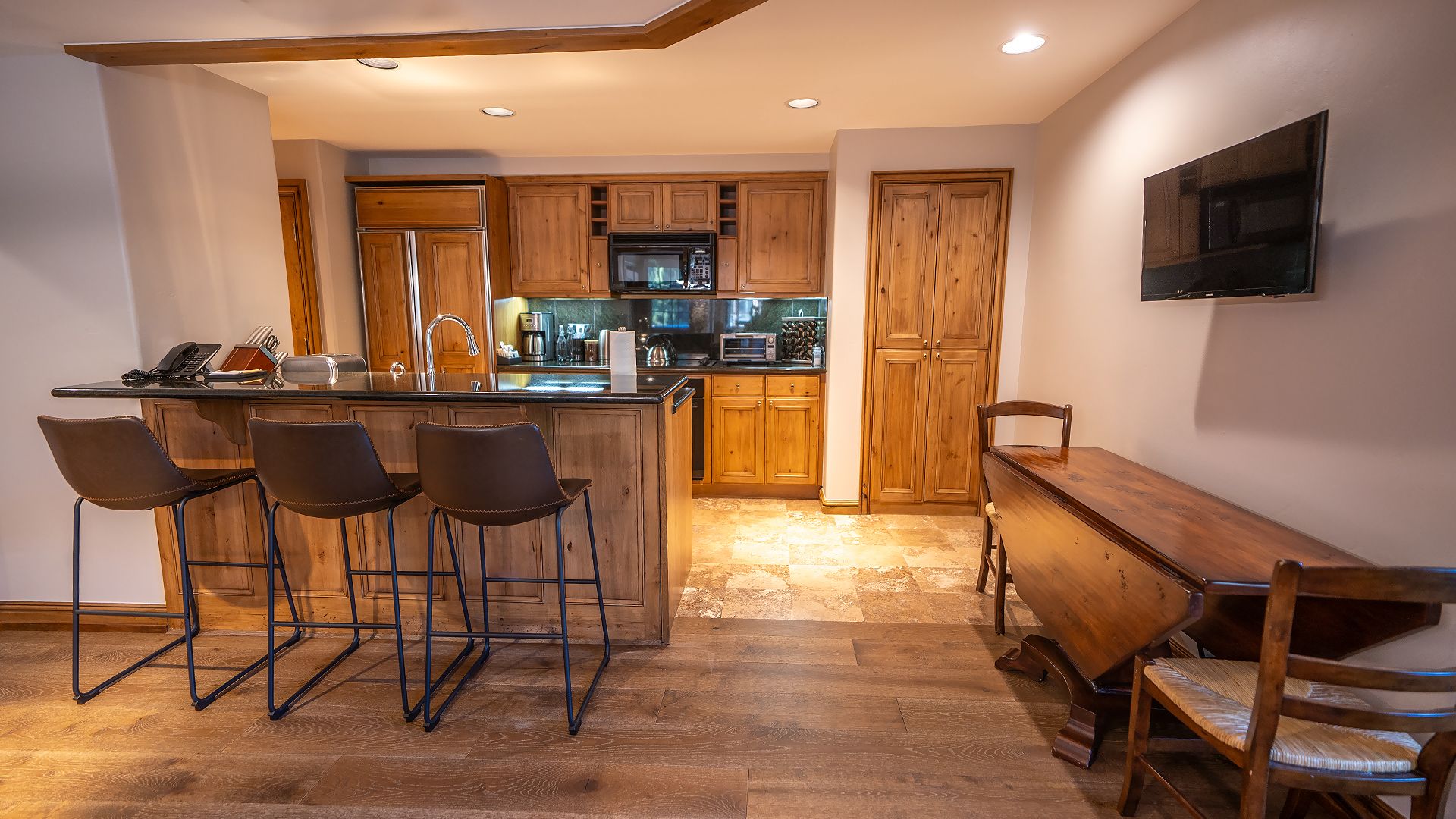 A modern kitchen with wooden cabinets, a central island with bar stools, and a dining table.