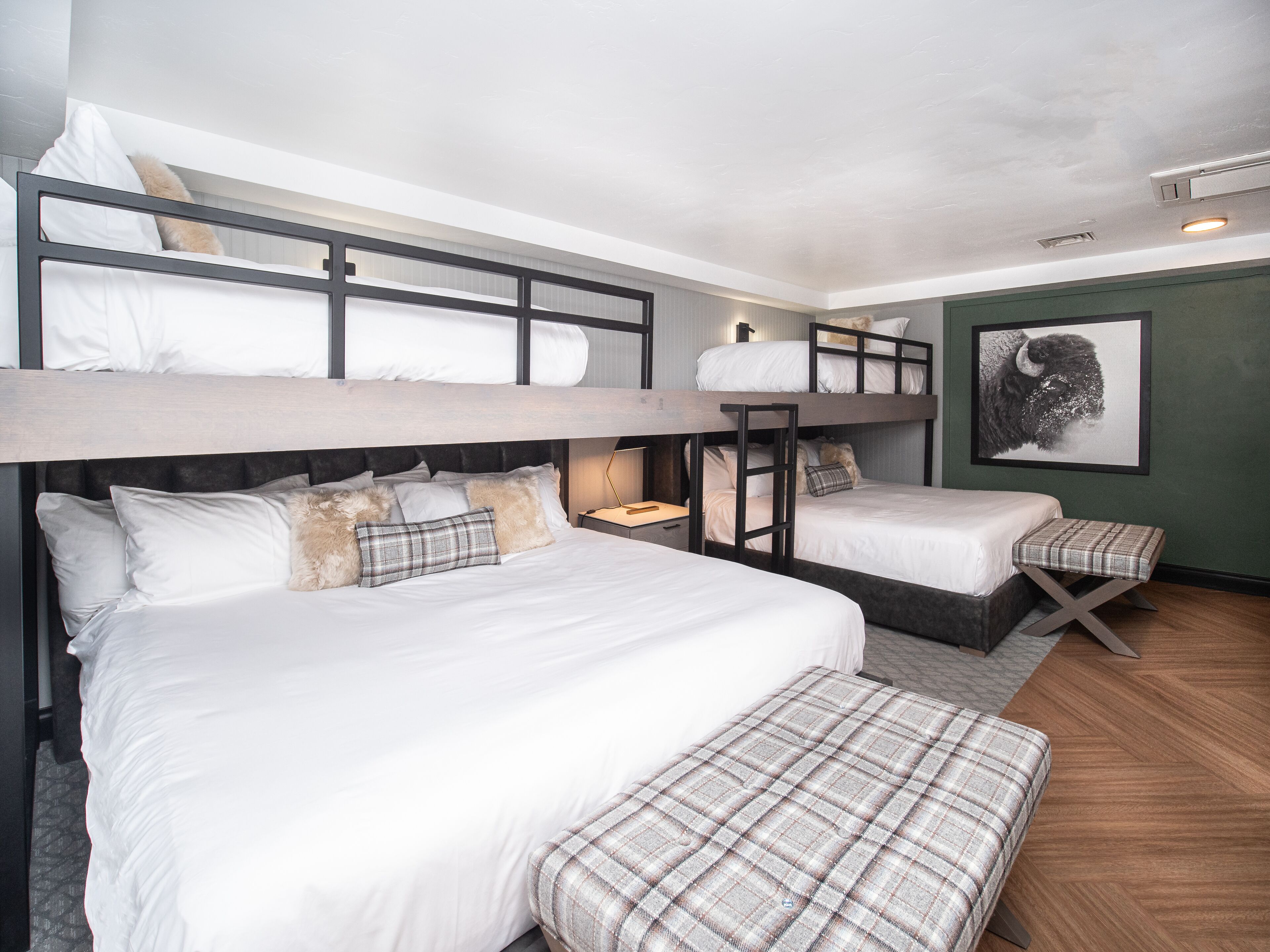 A bunk bed room with a wooden headboard, a bedside table with a lamp, and a framed picture on the wall.