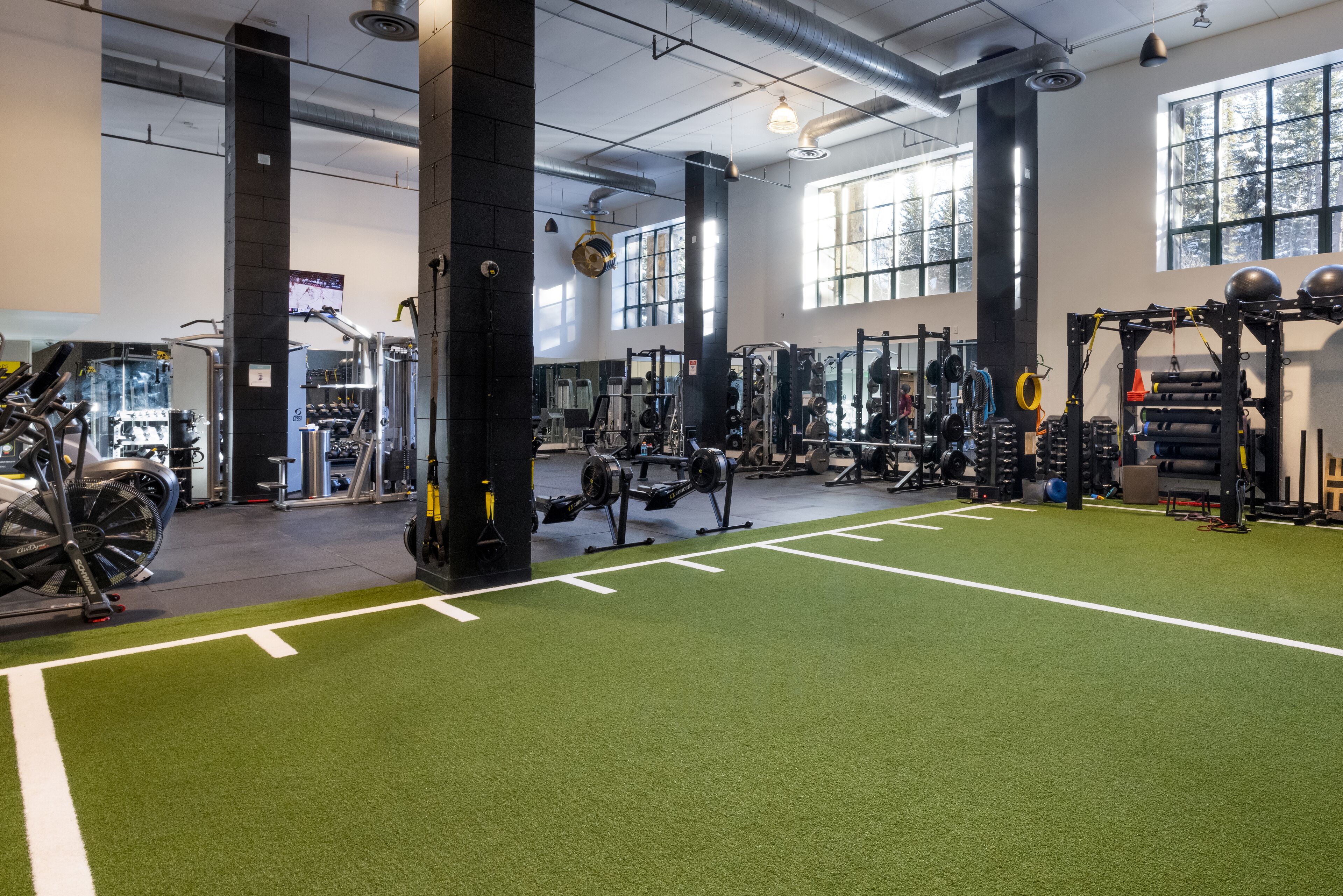 A gym with green flooring, weightlifting equipment, and large windows.