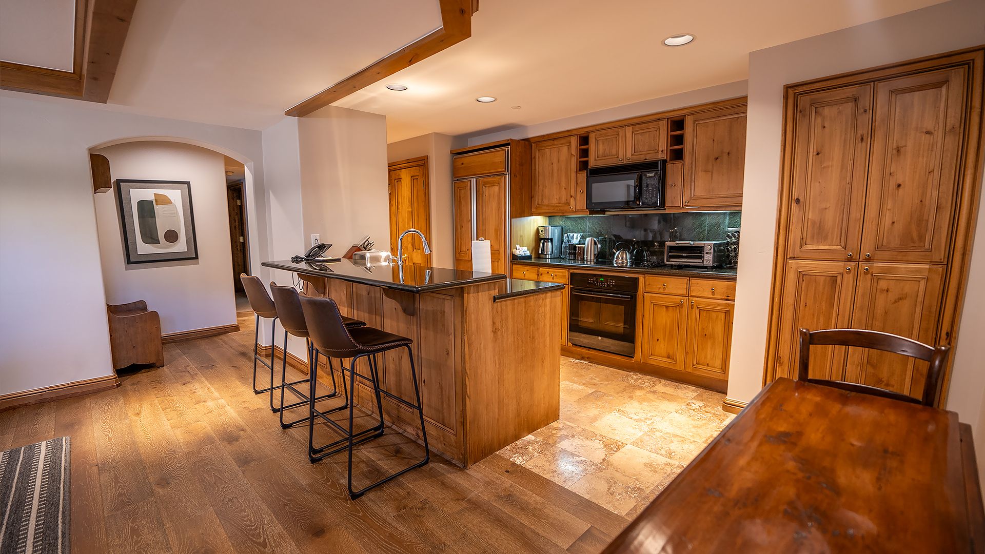 A modern kitchen with wooden cabinets, a central island with bar stools, and a dining table.
