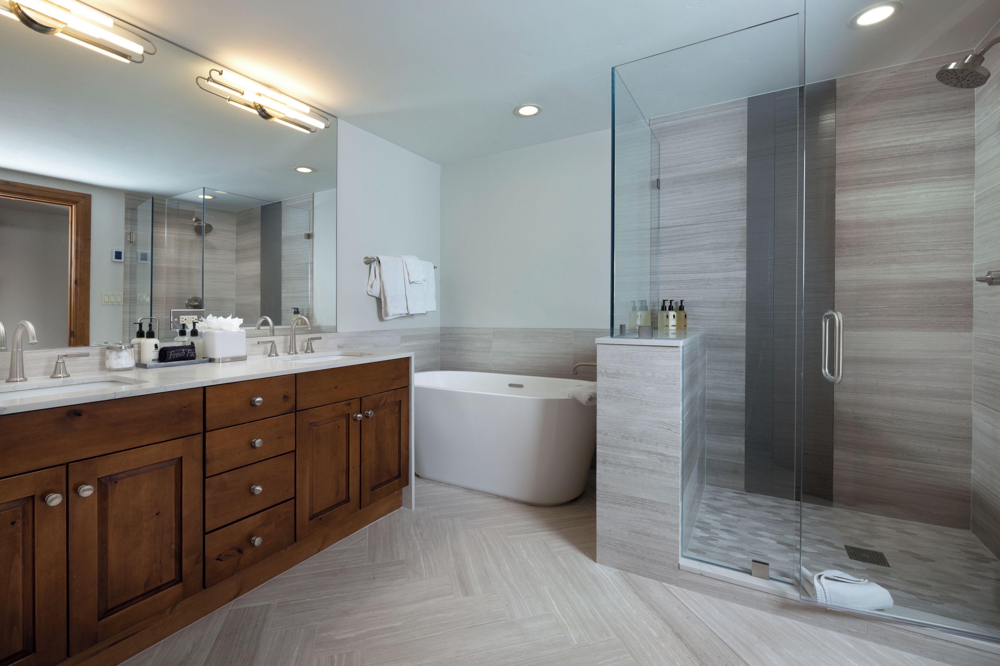A modern bathroom with a glass-enclosed shower, a freestanding bathtub, and a double vanity with wooden cabinets.