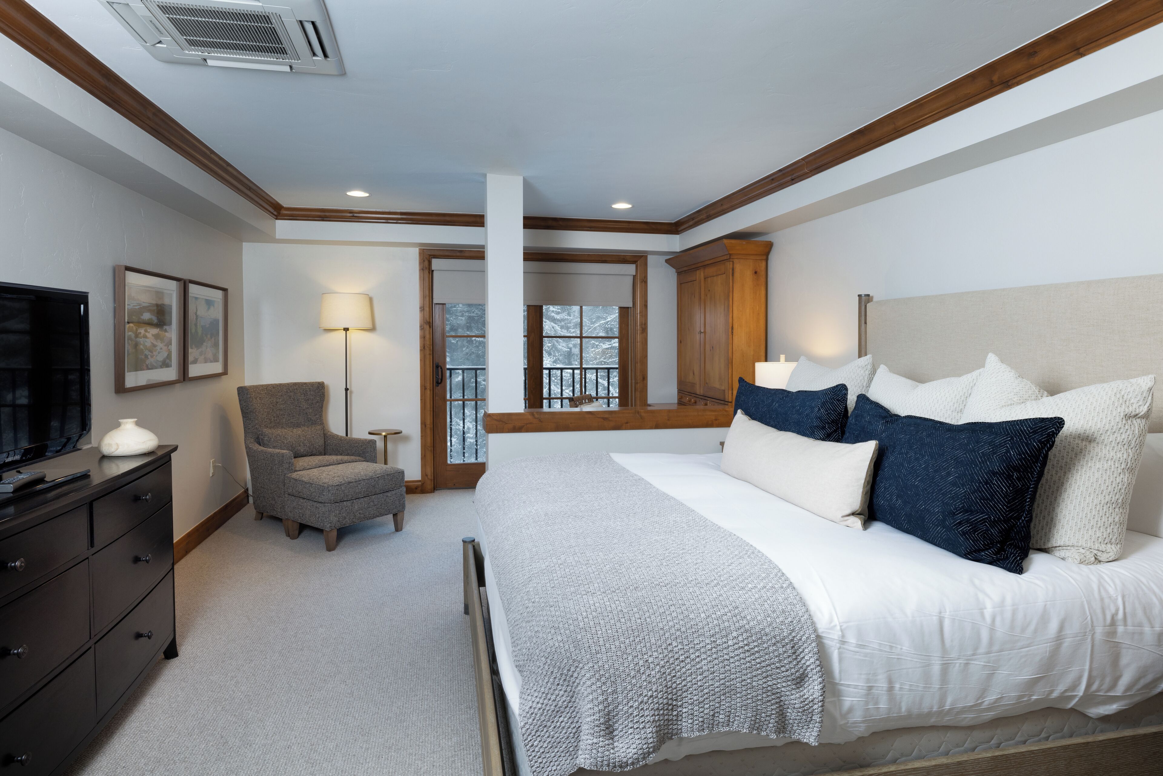 A bedroom with a large bed, a chair, a dresser, and a television.