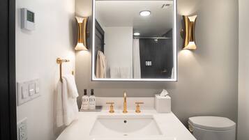 Ein modernes Badezimmer mit großem Spiegel, weißem Waschbecken, goldenen Armaturen und Toilette.