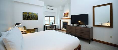 A hotel room with a large bed, a desk with a chair, a television, a fireplace, and a large mirror.